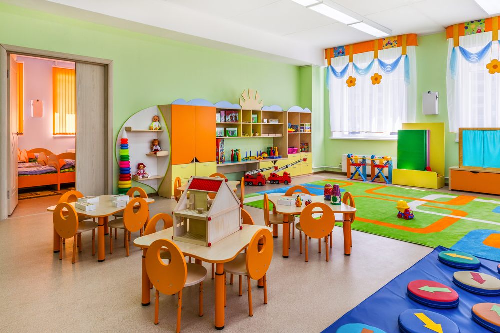 Aula de escuela infantil con mesas bajas, estanterías y zona de juego
