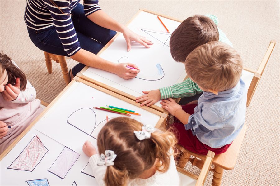 Niños dibujando alrededor de una mesa con lápices de colores